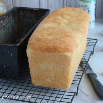 A loaf of homemade white bread on a cake rack.