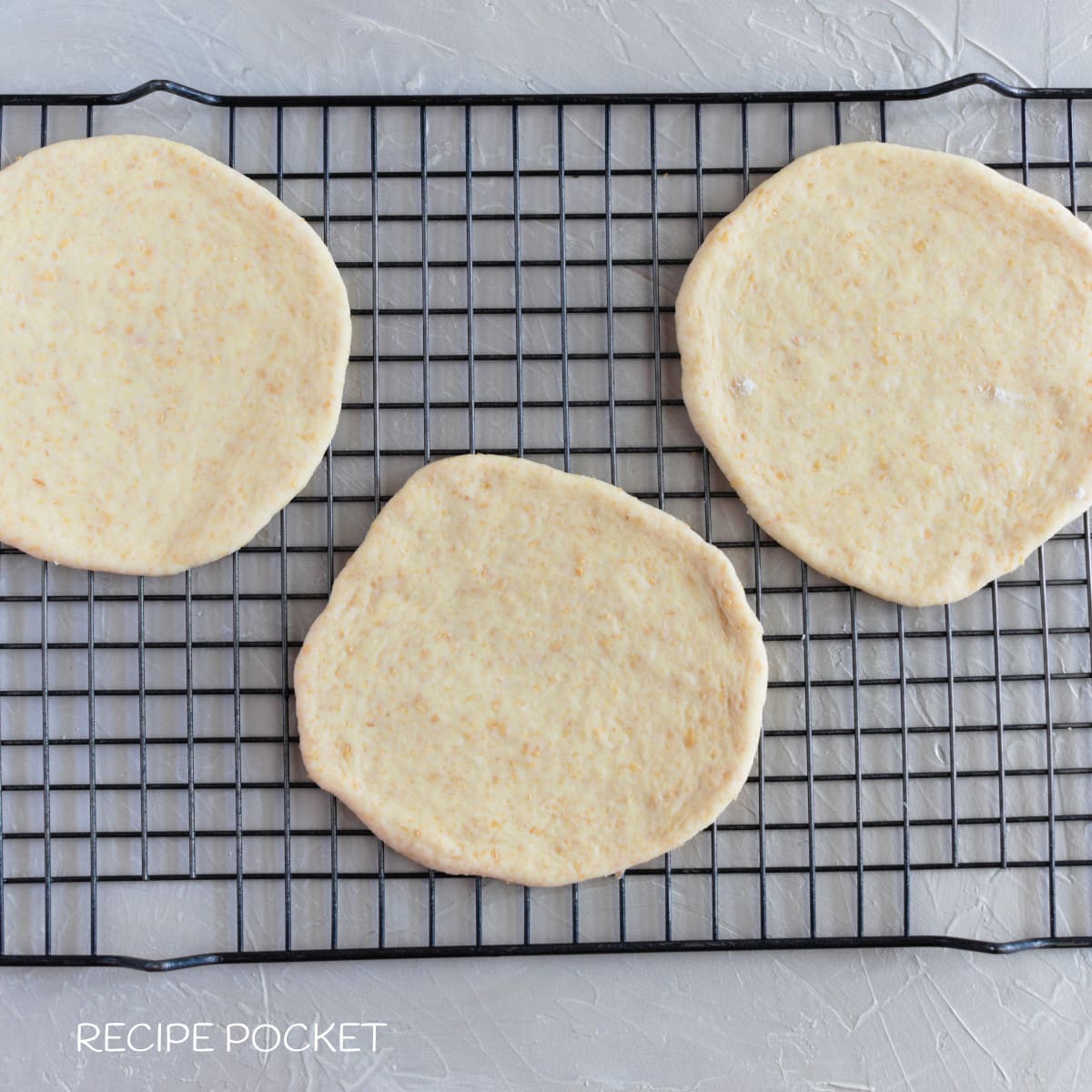 Unbaked pita bread dough on a cake rack.