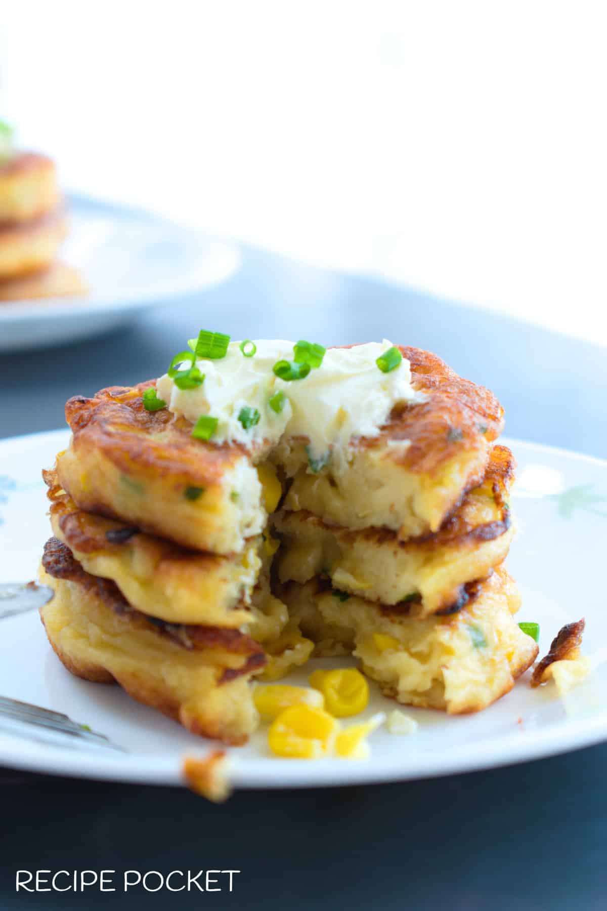 A stack of cut creamy corn fritters with sour cream and chives on top.