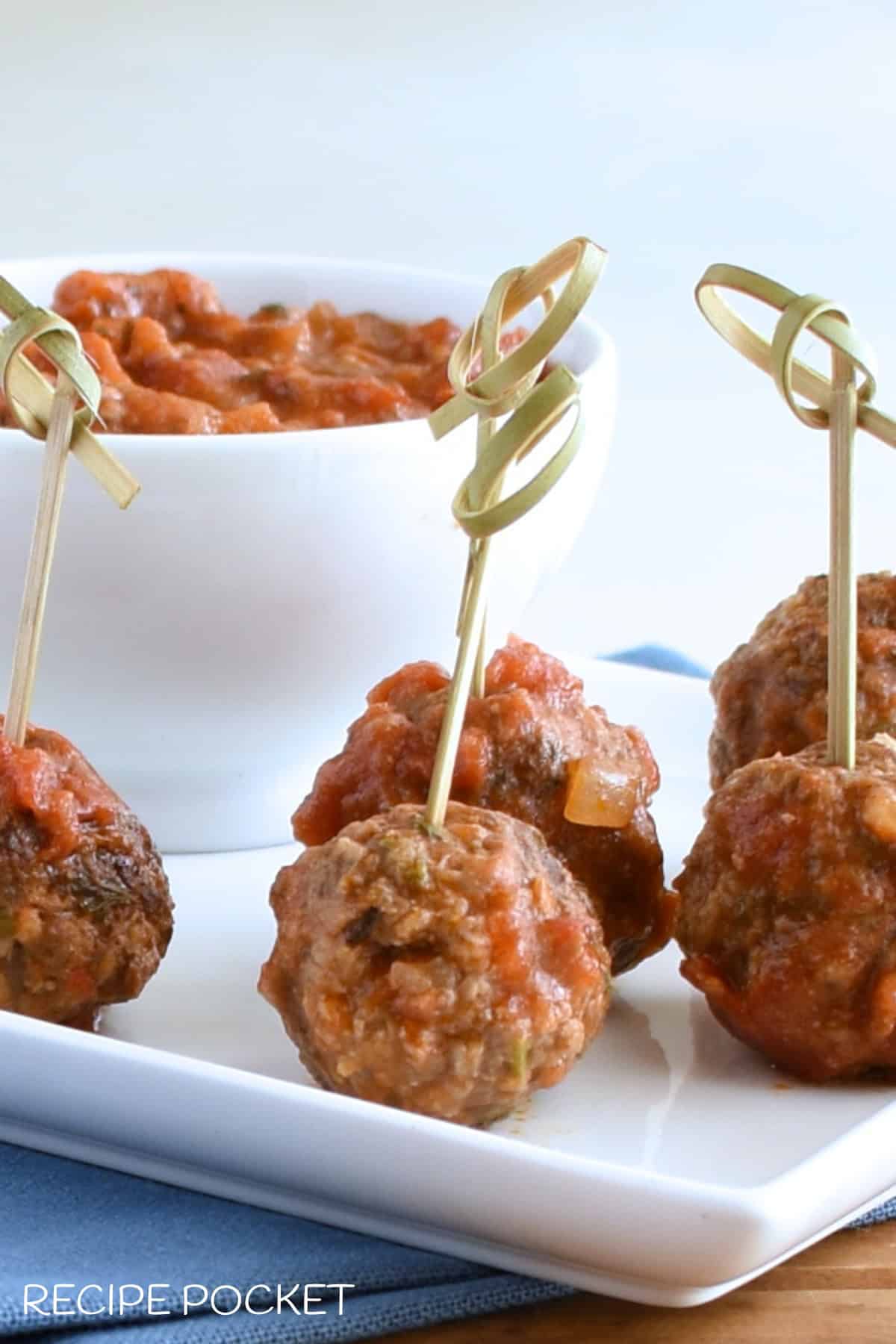 Meatballs on a plate with a bowl of sauce.